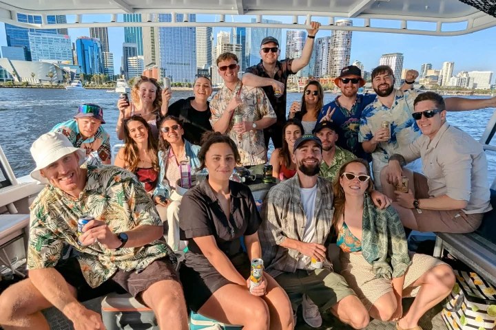 Group of people smiling on a boat with city skyline in the background.