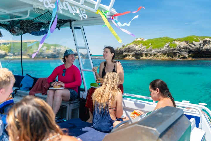 People eating on a boat with blue water and rocky island background on a sunny day.