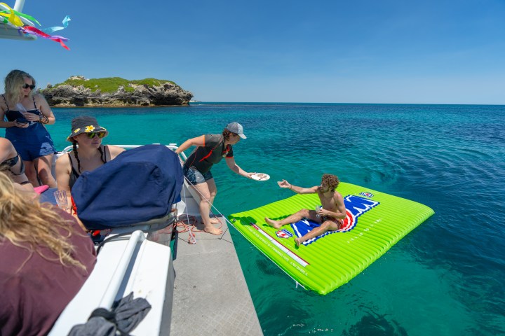 People enjoying a sunny day on a boat and raft in clear blue ocean.