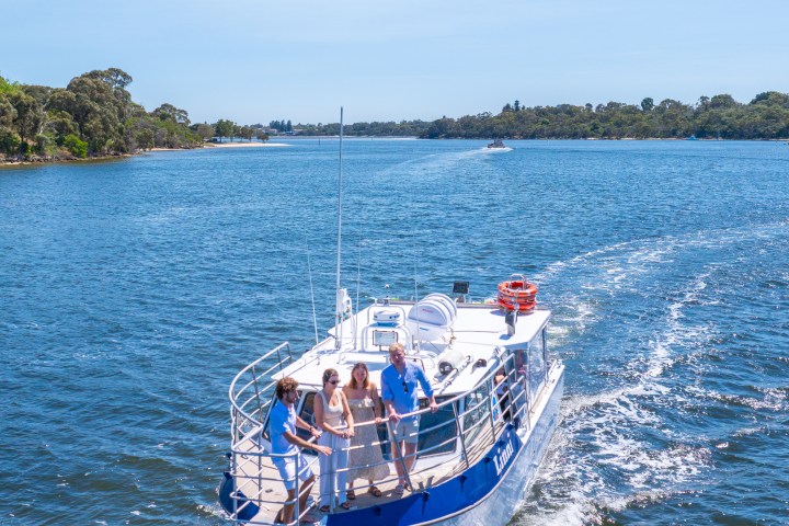Four people on a boat cruising on a sunny day in a wide river.