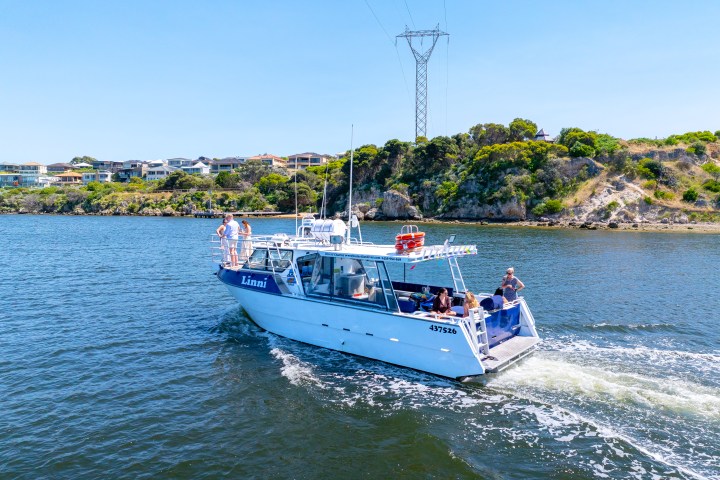 White boat named Linni on water with people, homes, and trees in the background.