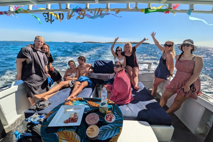 Group enjoying a boat party with snacks, drinks, and a 'Happy B-day' banner over blue ocean water.