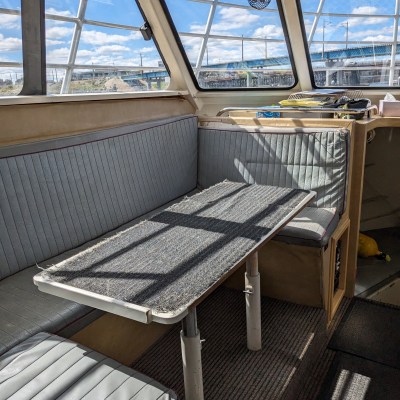 Interior of a boat with gray seating, table, and large windows showing a bright sky.