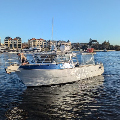 Small white boat on water near buildings under clear blue sky.