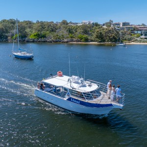 Boat named 'Linni' with passengers on a river, surrounded by trees and houses.