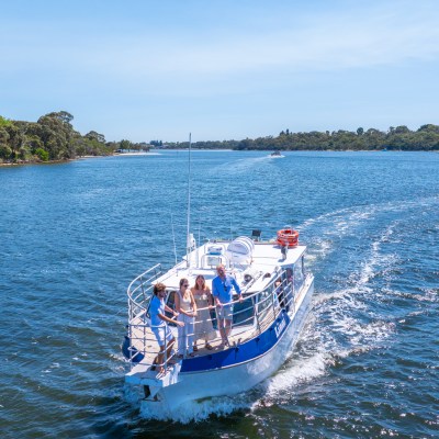 A small boat with four people sailing on a blue river under a clear sky.
