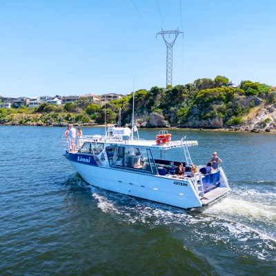 Motorboat with people cruising on a river, with houses and green vegetation in the background.